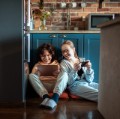 Close up of a young brother and sister using their mobile devices in the kitchen.
